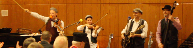 Ingo zeigt mit dem Geigenbogen ins Publikum, Véronique spielt Geige, Andreas lächelt Gitarre spielend ins Publikum und Jochen mit Hut spielt den Bass.