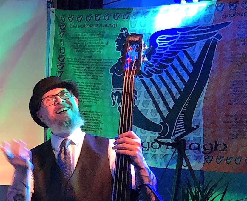 Jochen Blachucinski mit seinem E-Bass, im Hintergrund die irische Fahne mit dem Text der Nationalhymne und einer Harfen-Frauen-Bild-Kombination